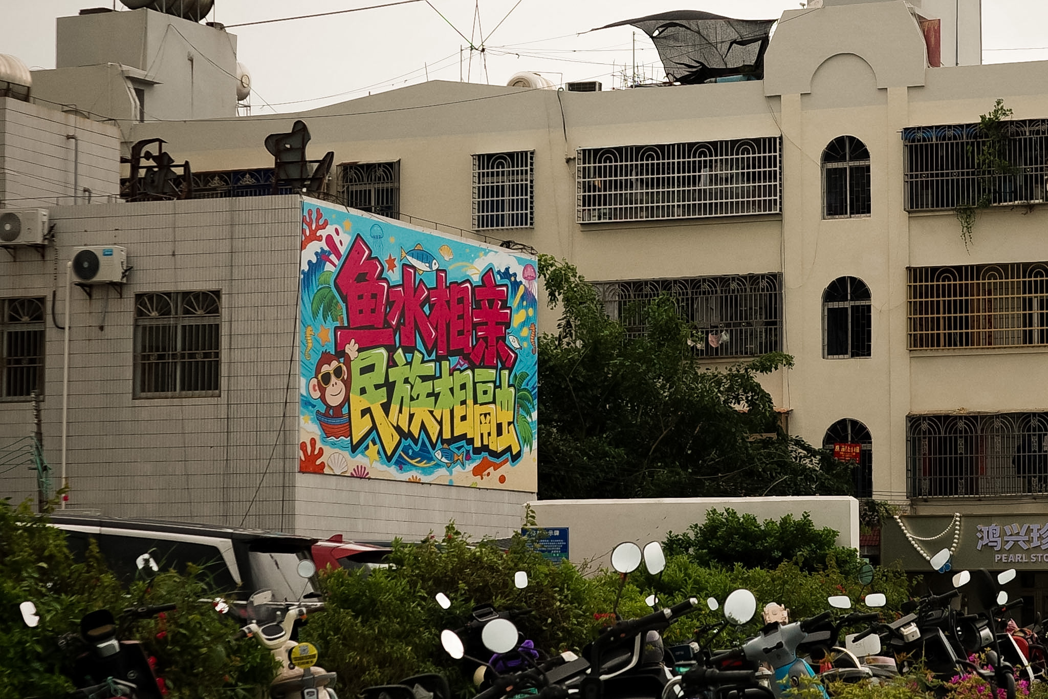 A bright cartoon mural on a tiled building wall reading, in Chinese, fish and water fall in love, ethnicities merge as one.